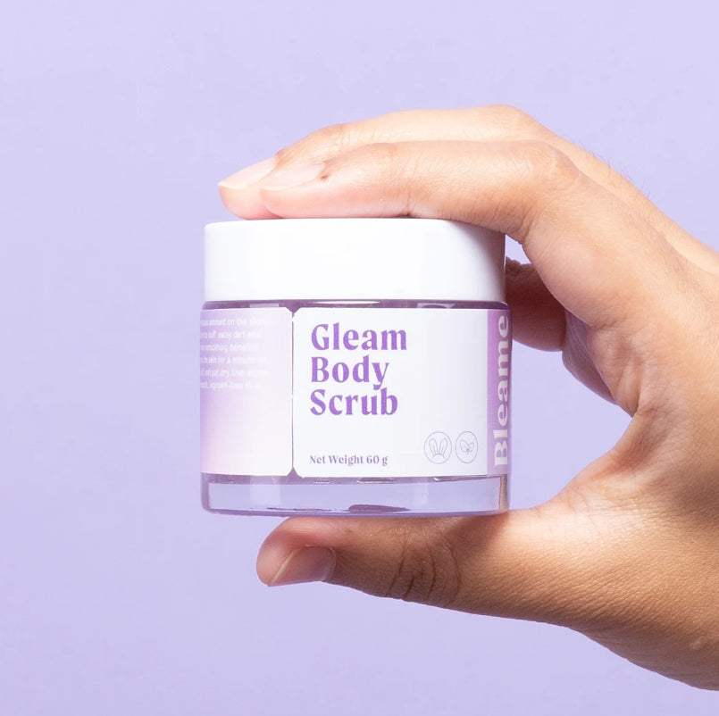 Lumi Gleam Body Scrub jar held against a light purple background.
